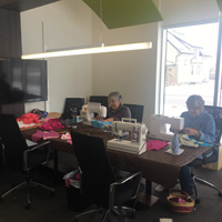 Ladies sewing masks and capes on large wooden table